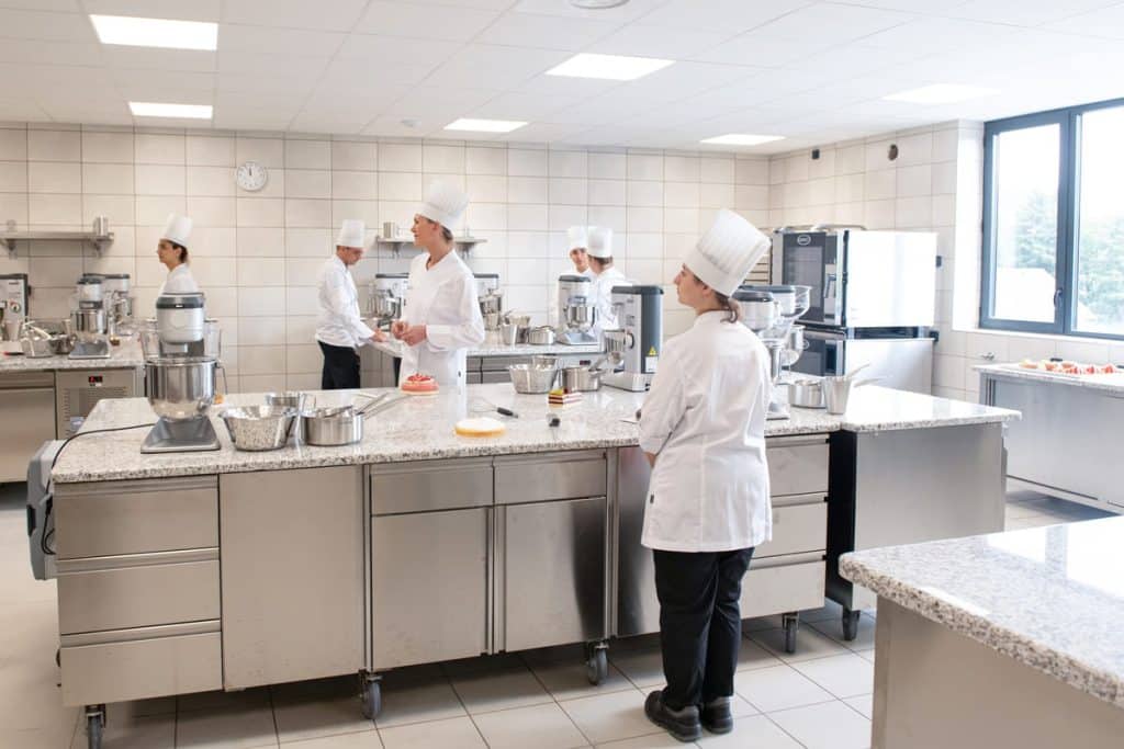 culinary students in classroom kitchen taking instruction from chef